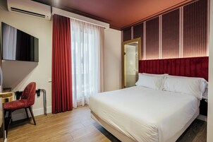 Una habitación de hotel con cama, escritorio, silla, televisor y ventana con cortinas.