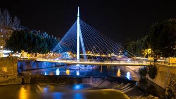 A nighttime view of a modern bridge with a central tower, surrounded by water and trees.