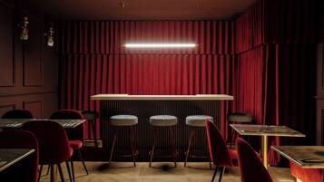 Una zona de bar con cortinas rojas, taburetes y mesas.