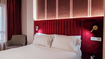 Una habitación de hotel con una cama grande, una silla, un cabecero rojo y una ventana con cortinas.