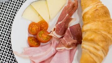 A breakfast plate with croissant, cheese, tomatoes, and prosciutto.