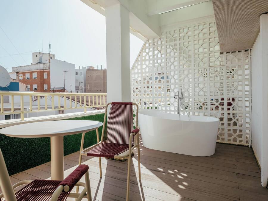 Un balcón con una mesa redonda, dos sillas, una bañera blanca y un panel de celosía decorativo blanco.