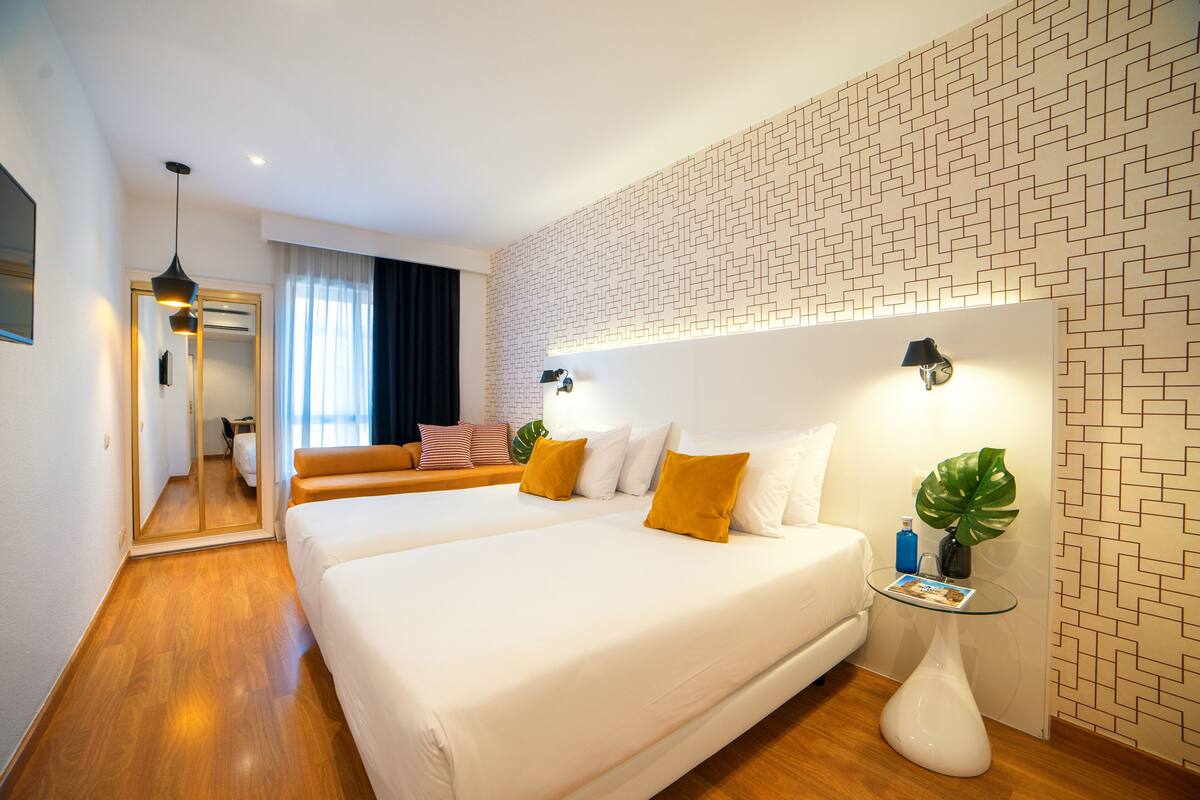 Une chambre d’hôtel moderne avec un grand lit, une table d’appoint en verre, un miroir et une vue sur le couloir.