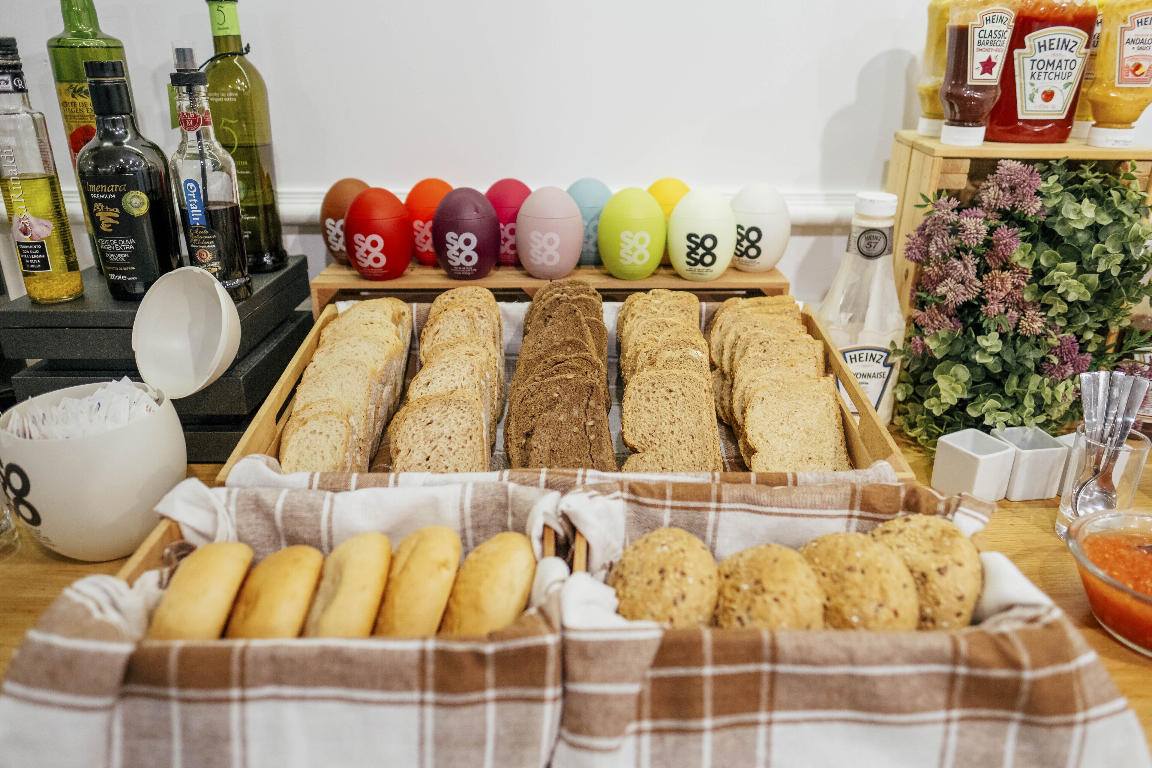 Variedad de panes y pasteles sobre una mesa, con botellas de salsas y un tazón de harina cerca.