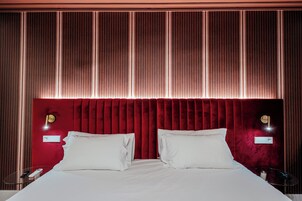 Una habitación de hotel con una cama grande, cabecera roja y dos mesitas de noche con lámparas.