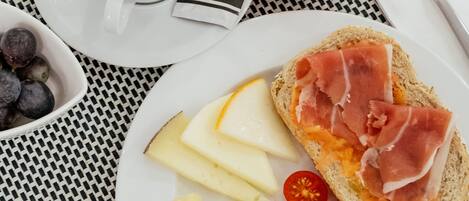 Un desayuno con una taza de café, un vaso de zumo de naranja, y un plato con pan, queso, tomates y huevos.