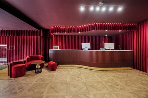 A reception area with a curved desk, red upholstered chairs, and a herringbone patterned floor. - Hotel Cetina Murcia (Murcia)
