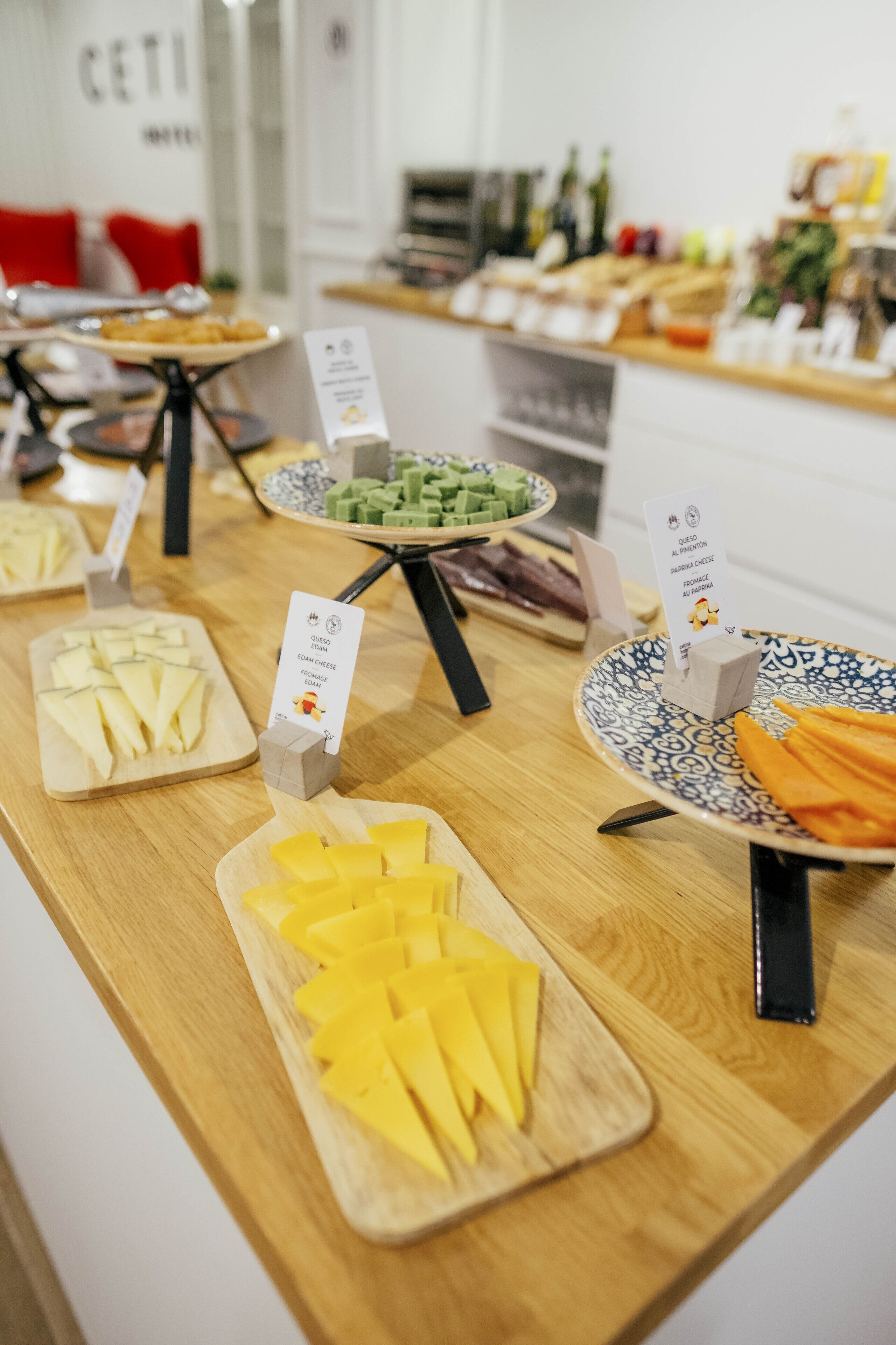 A buffet table with various cheese and vegetable platters, each labeled with a card.