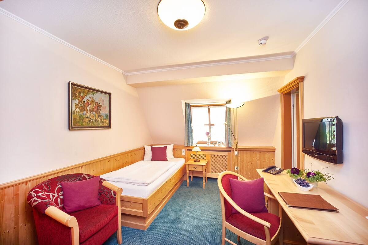 Ein Hotelzimmer mit einem Bett, einem Schreibtisch mit Stuhl, einem Fernseher und einem Bild an der Wand.