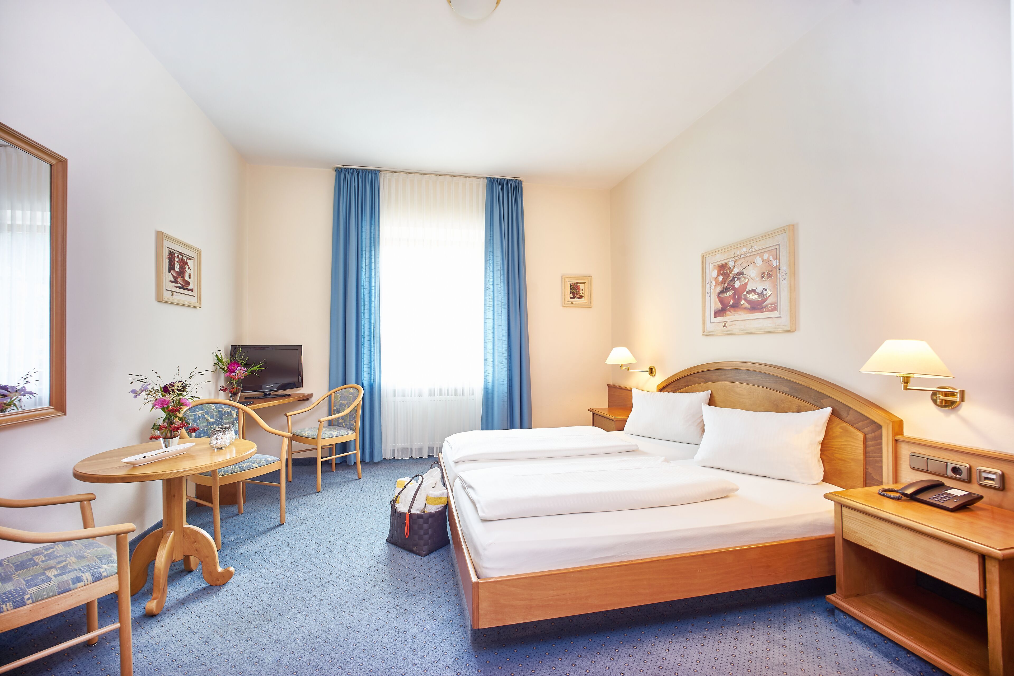 A hotel room with a bed, a desk, a chair, a television, and a lamp.