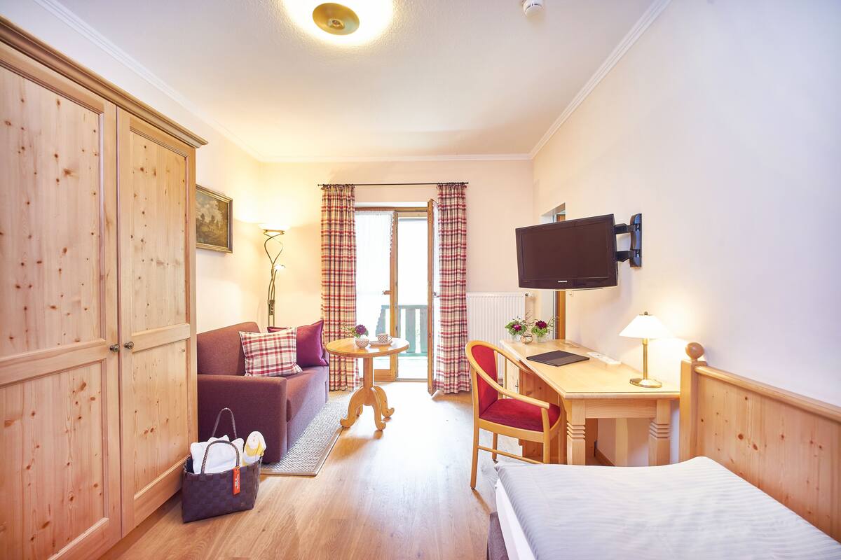 Ein Hotelzimmer mit Holzschrank, einer Couch, einem Schreibtisch mit Stuhl, einem Fernseher und einem Bett.