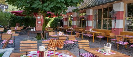 Un área de comedor al aire libre con mesas y sillas de madera, cubiertas con manteles a cuadros, y una variedad de comida y bebidas.