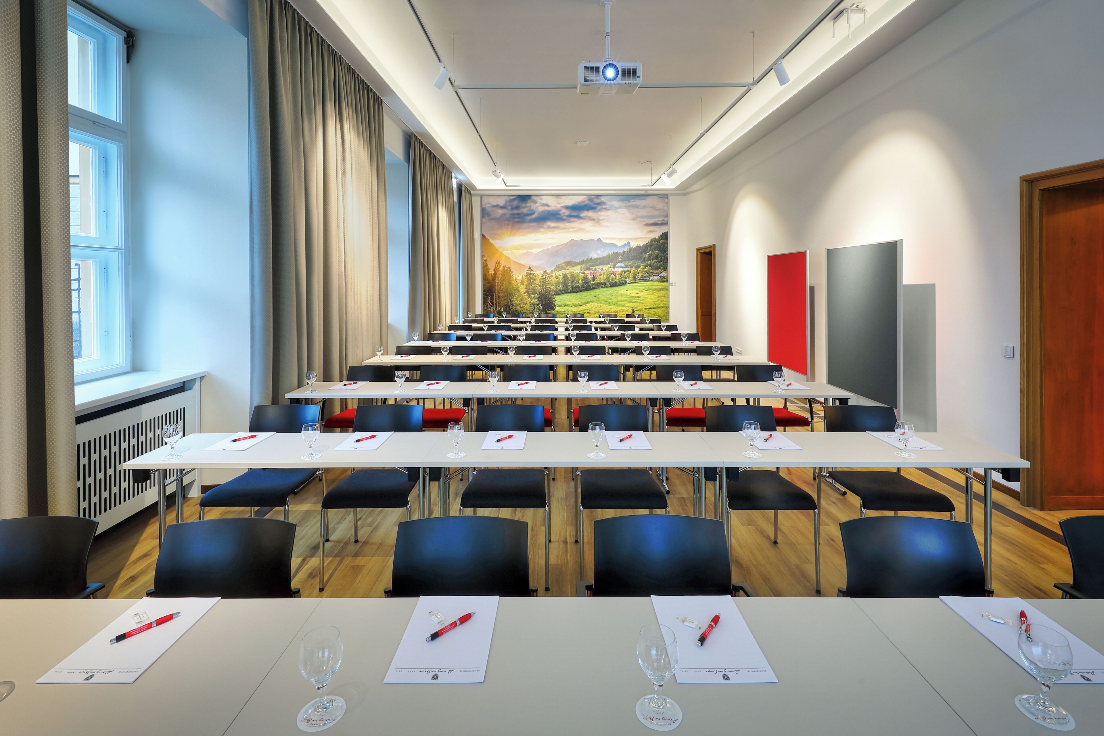 A conference room with a long table, chairs, and a projector screen.