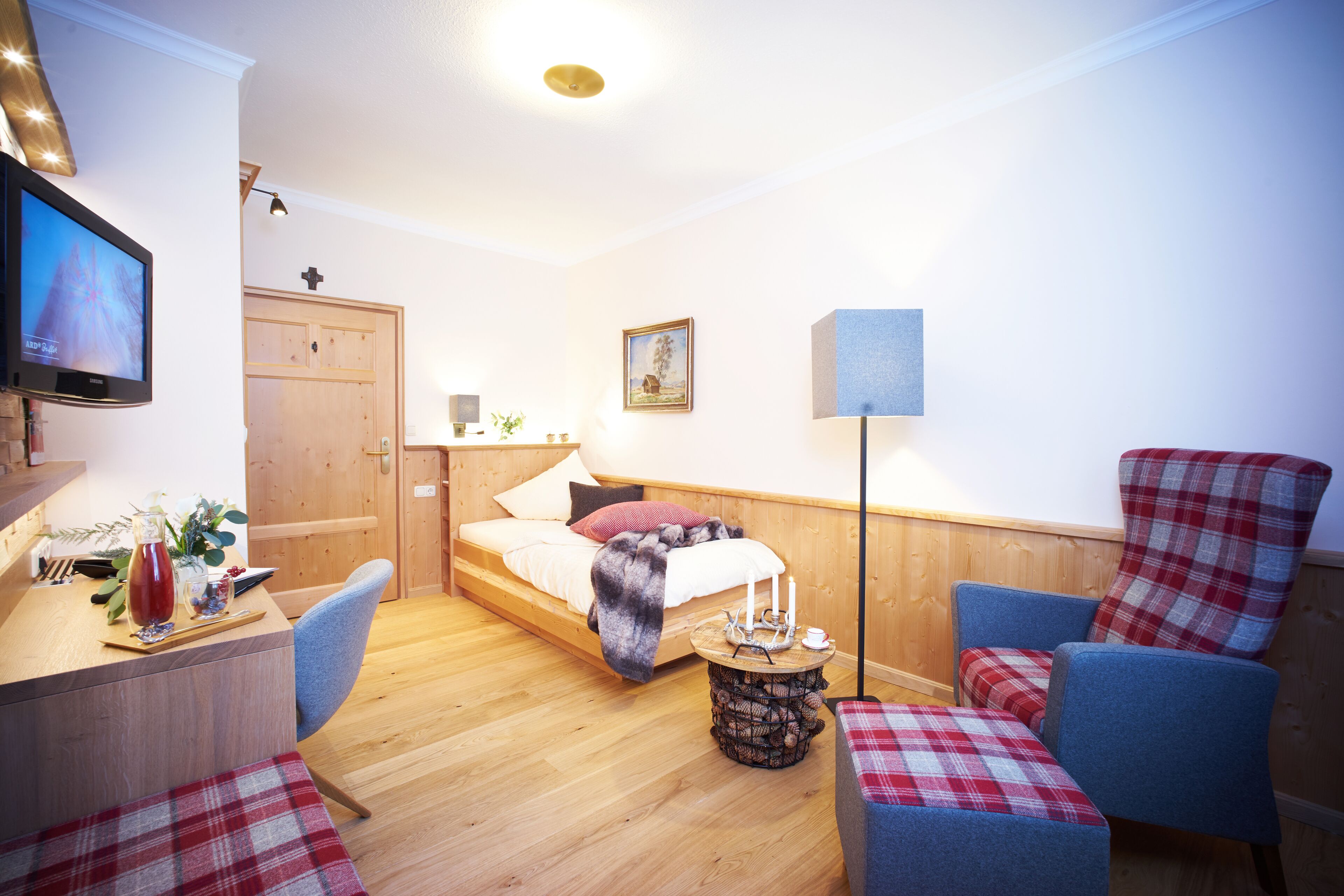 Ein gemütliches Zimmer mit einem Bett, einem Schreibtisch, einem Stuhl und einem kleinen Tisch mit einer Lampe.