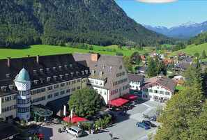 Un hotel con una torre, un patio interior y montañas al fondo.