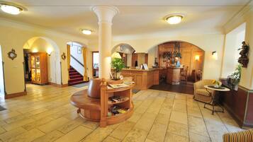 A spacious lobby with a central column, a reception desk, and a staircase leading to another area.