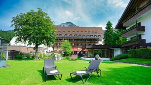 Une cour d’hôtel avec deux chaises longues, un arbre et une montagne en arrière-plan.