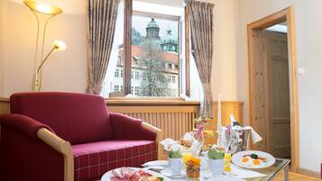 A dining area with a red sofa, a table set for breakfast, and a window with a view of a building.