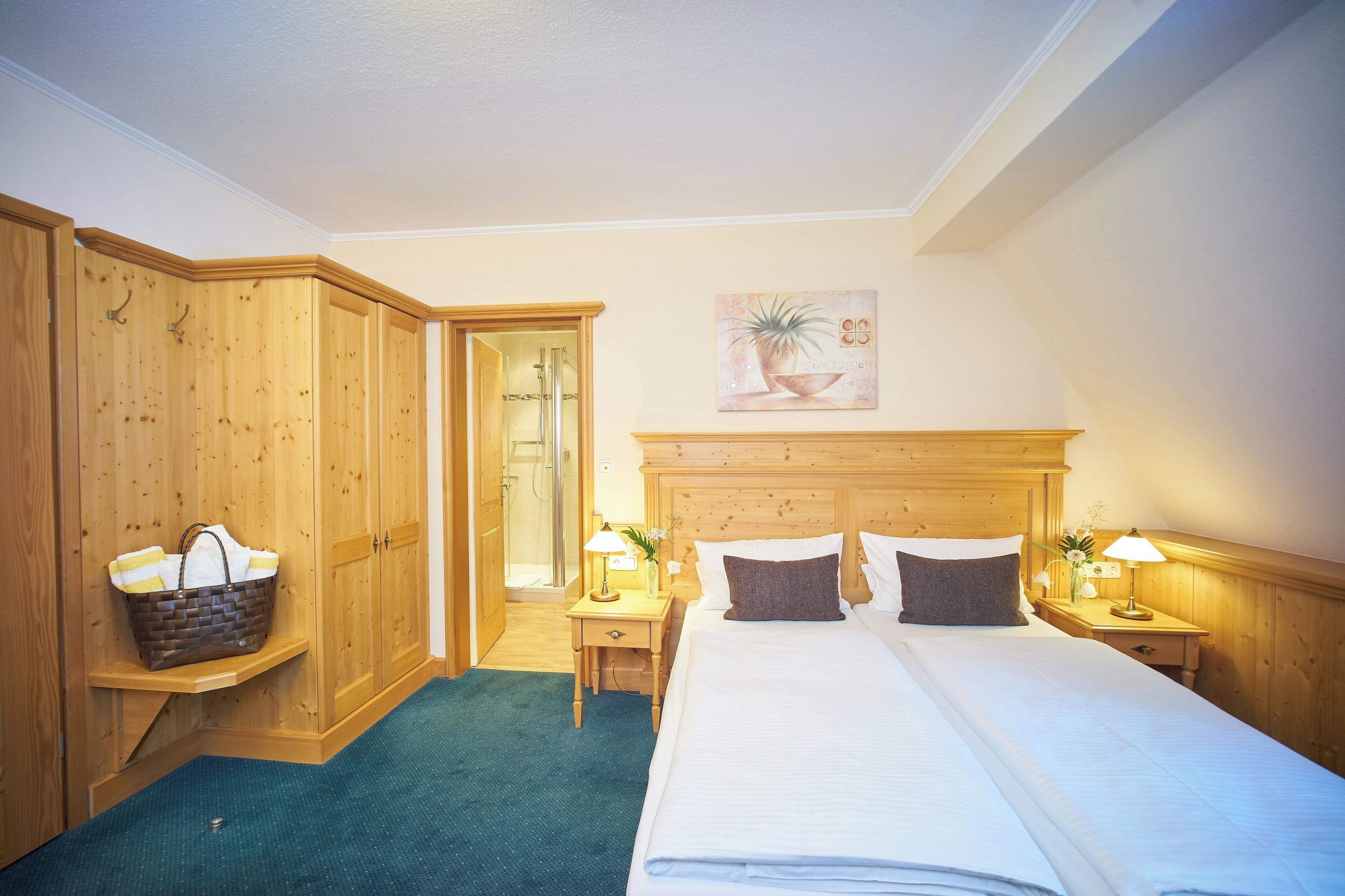 Habitación de hotel con armario de madera, cama con ropa de cama blanca, dos mesitas de noche con lámparas y un cuadro en la pared.