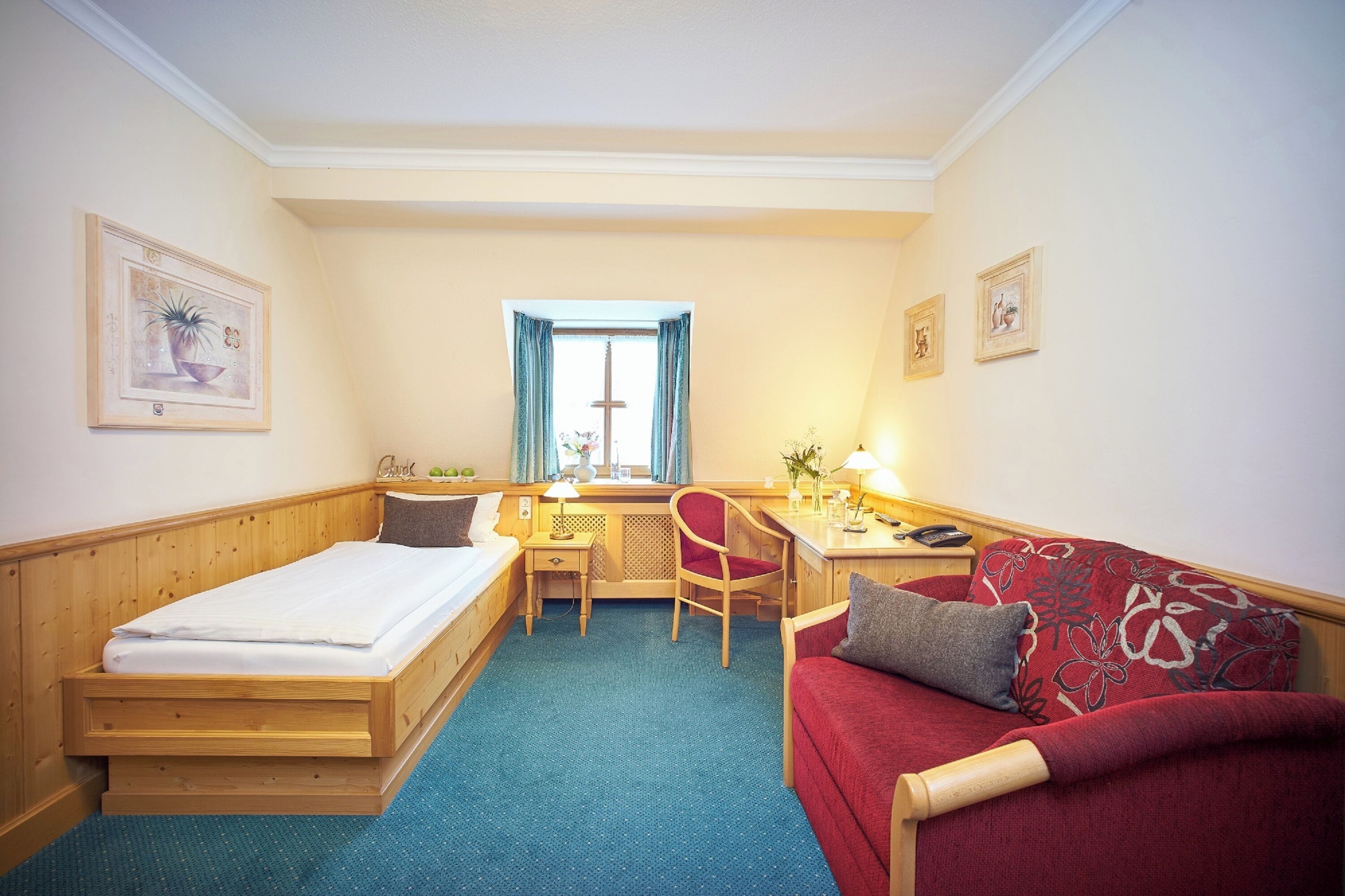 Een kleine hotelkamer met een enkel bed, een bureau, een stoel en een bank.