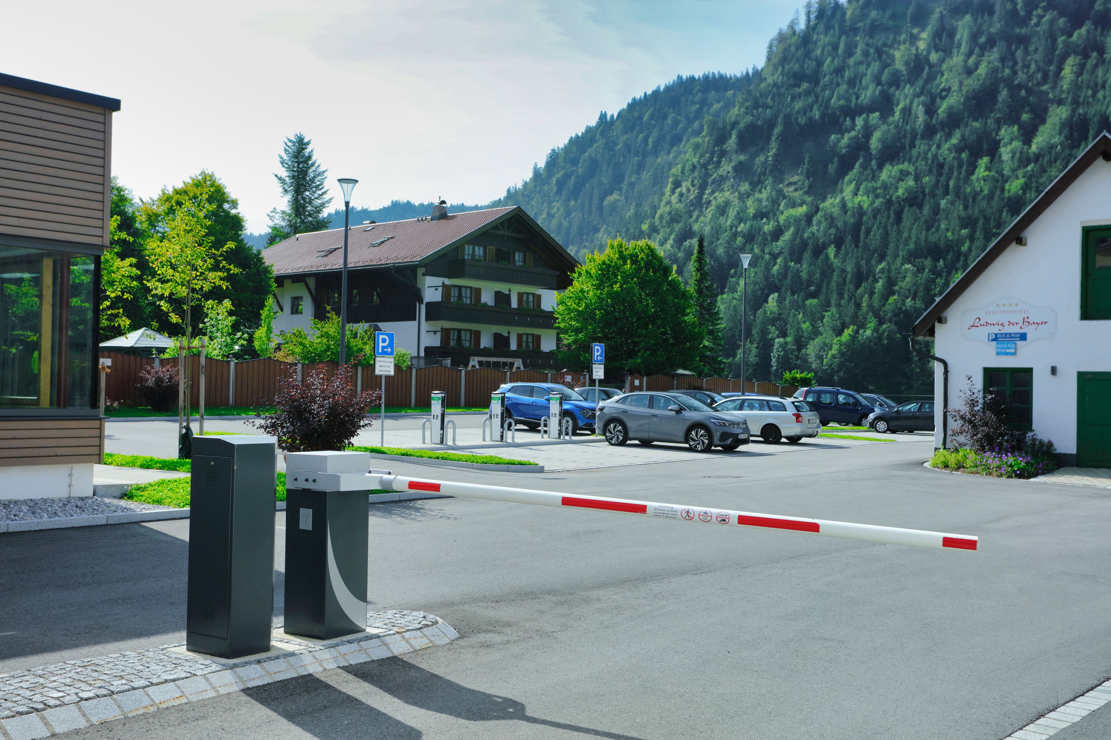 Un espace de stationnement avec des voitures, une entrée fermée par un portail et des bâtiments avec des panneaux indicateurs.
