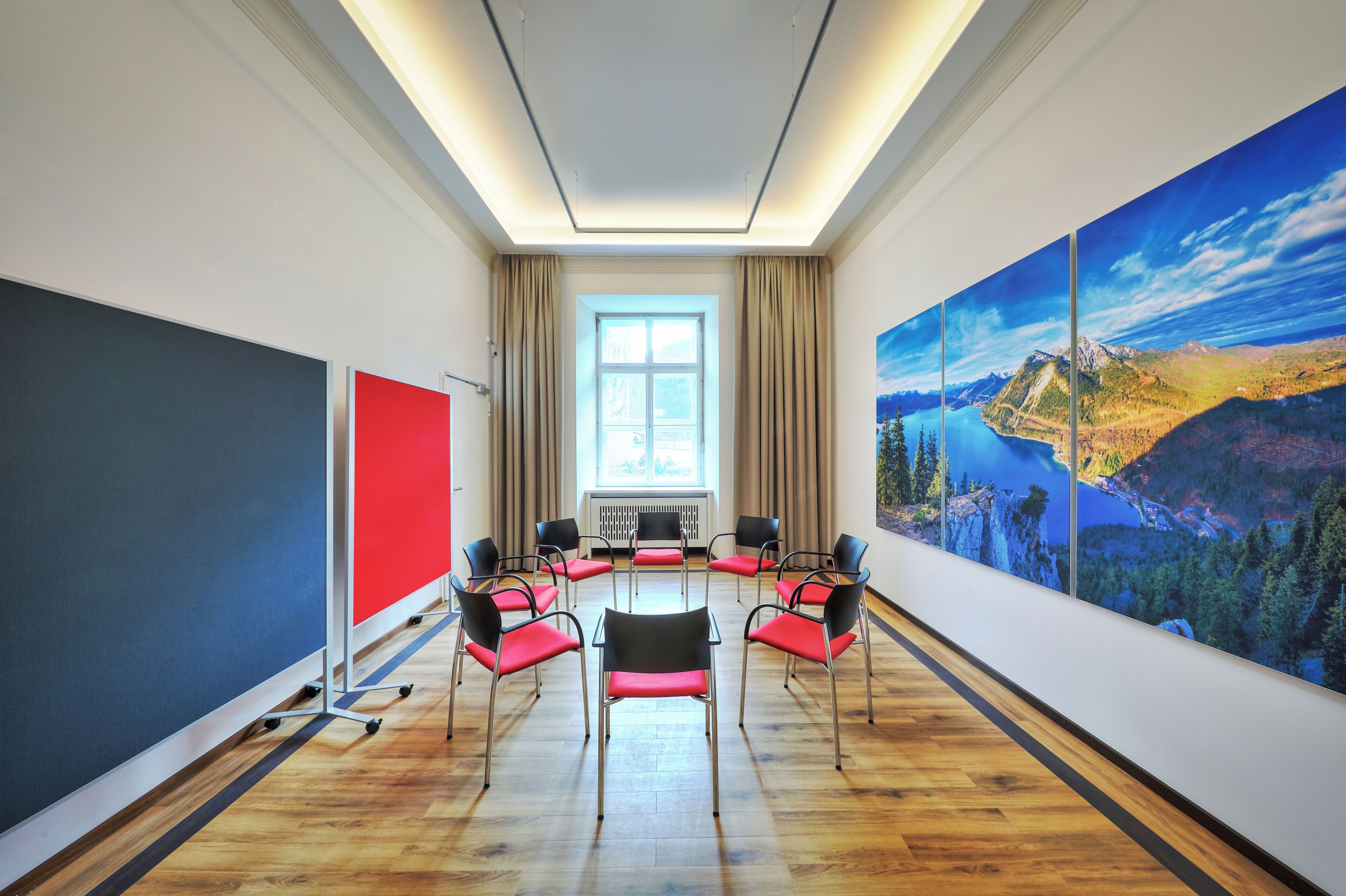 Un salón de conferencias con un ventanal grande, una pantalla roja y un cuadro pintoresco en la pared.