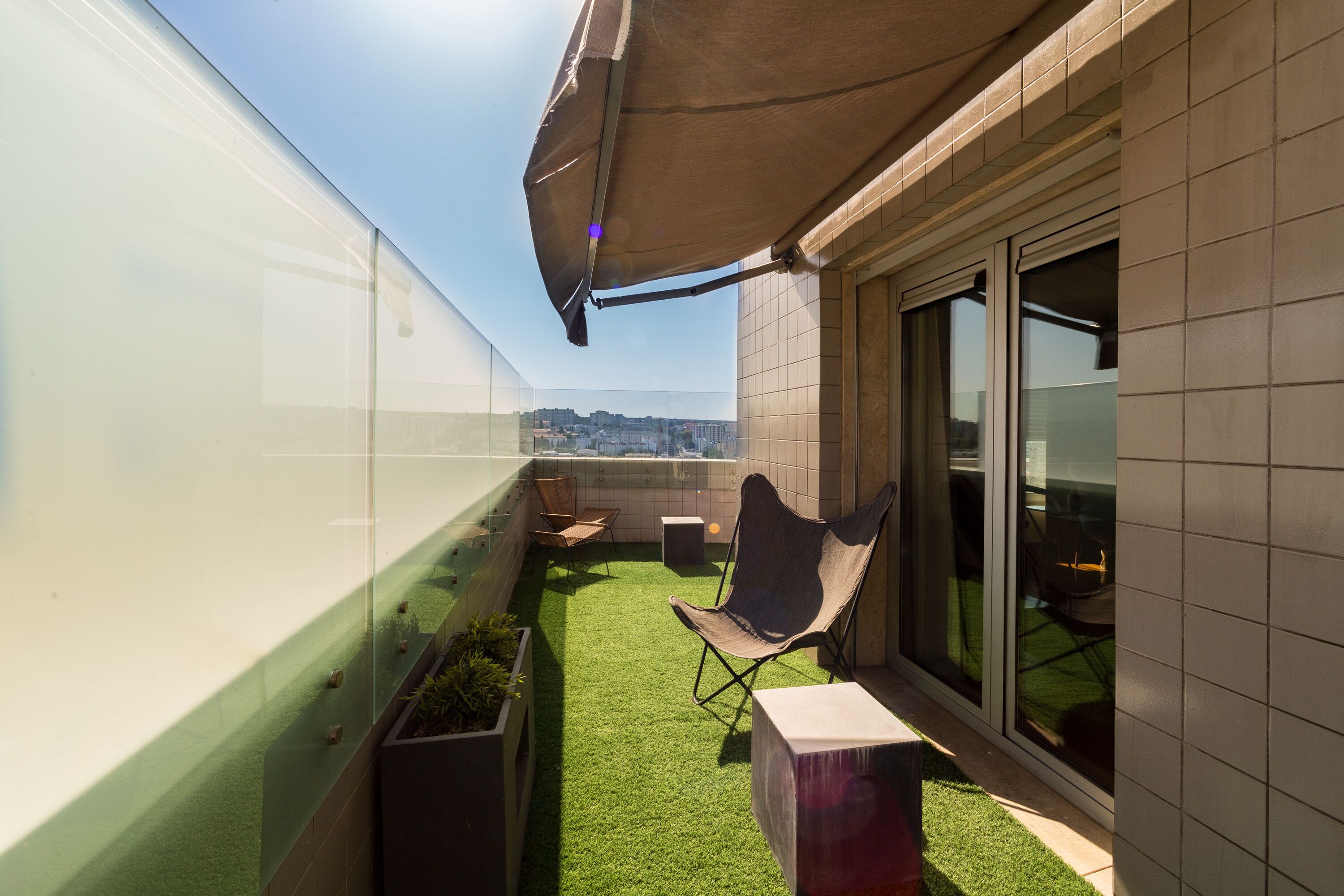 A rooftop terrace with artificial grass, a folding chair, a small table, and a glass partition.