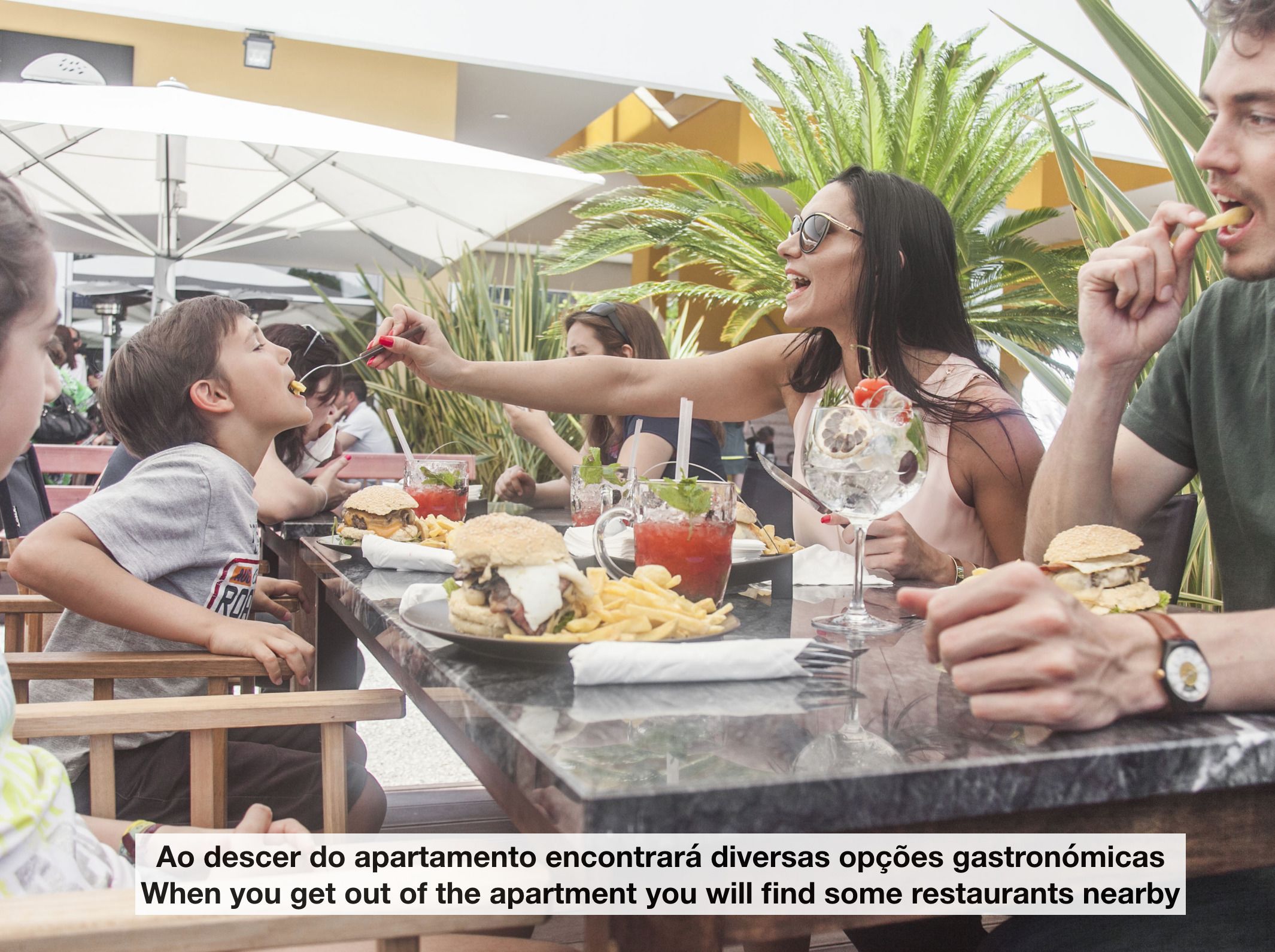Un grupo de personas cenando al aire libre en un restaurante, con varios platos y bebidas sobre la mesa.
