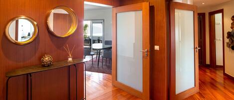 Un interior moderno con suelo de madera, una puerta de cristal y un espejo redondo en la pared.