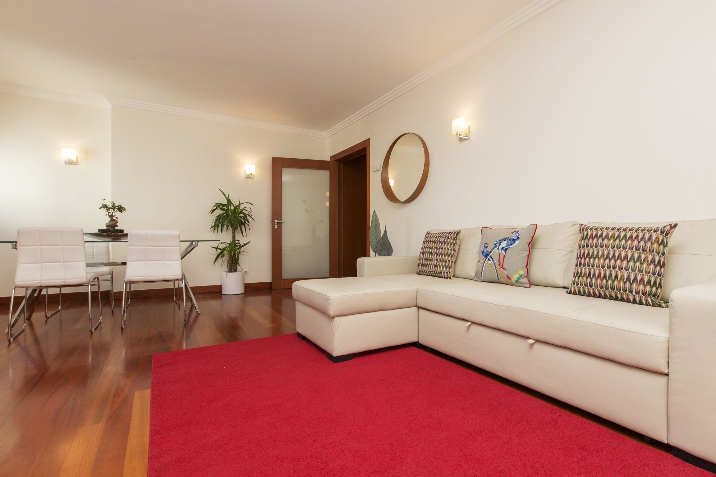 Una sala de estar moderna con un sofá modular, un tapete rojo y una mesa de centro de vidrio.