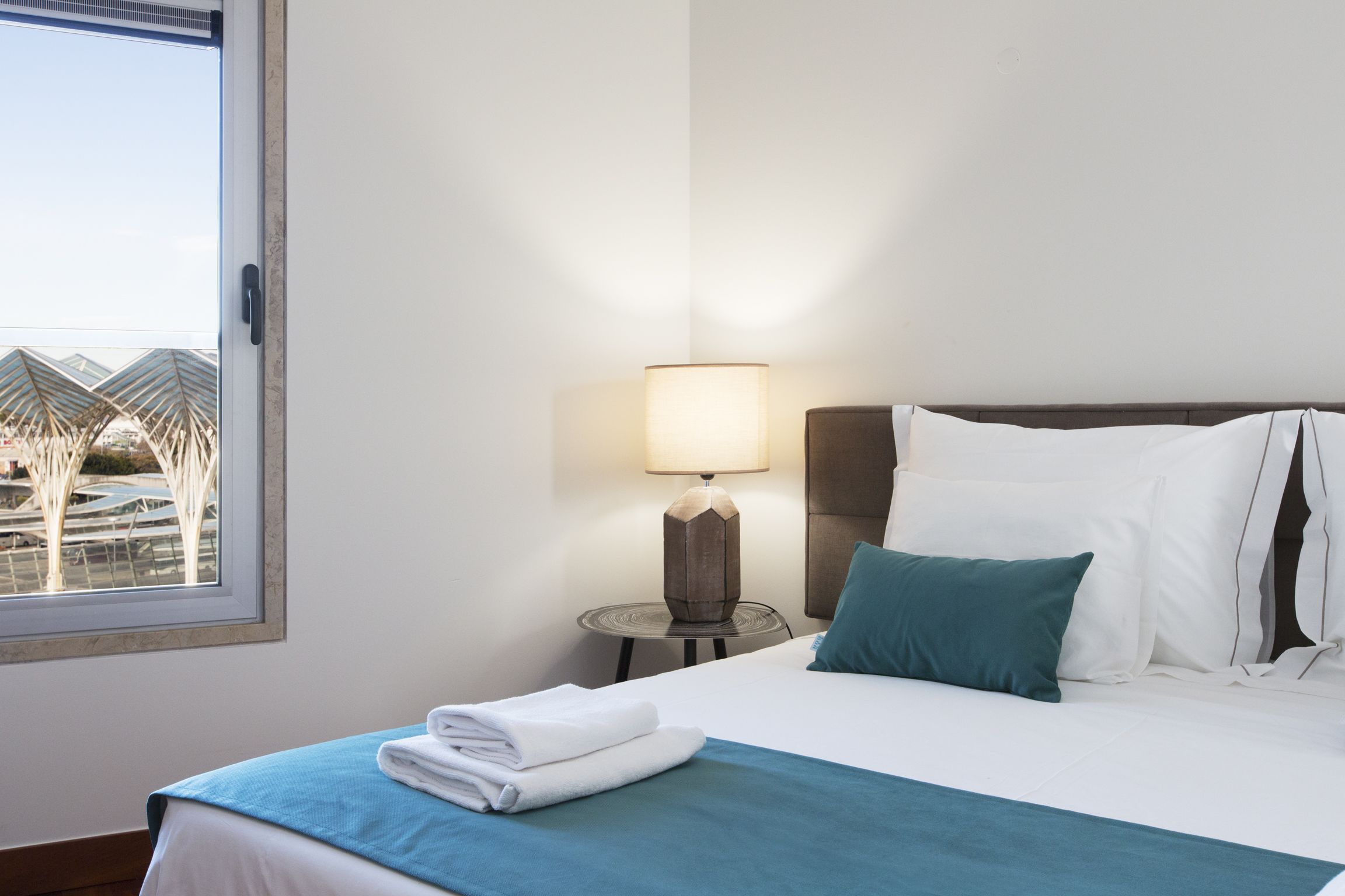 A hotel room with a bed, a lamp, and a view of a building outside.