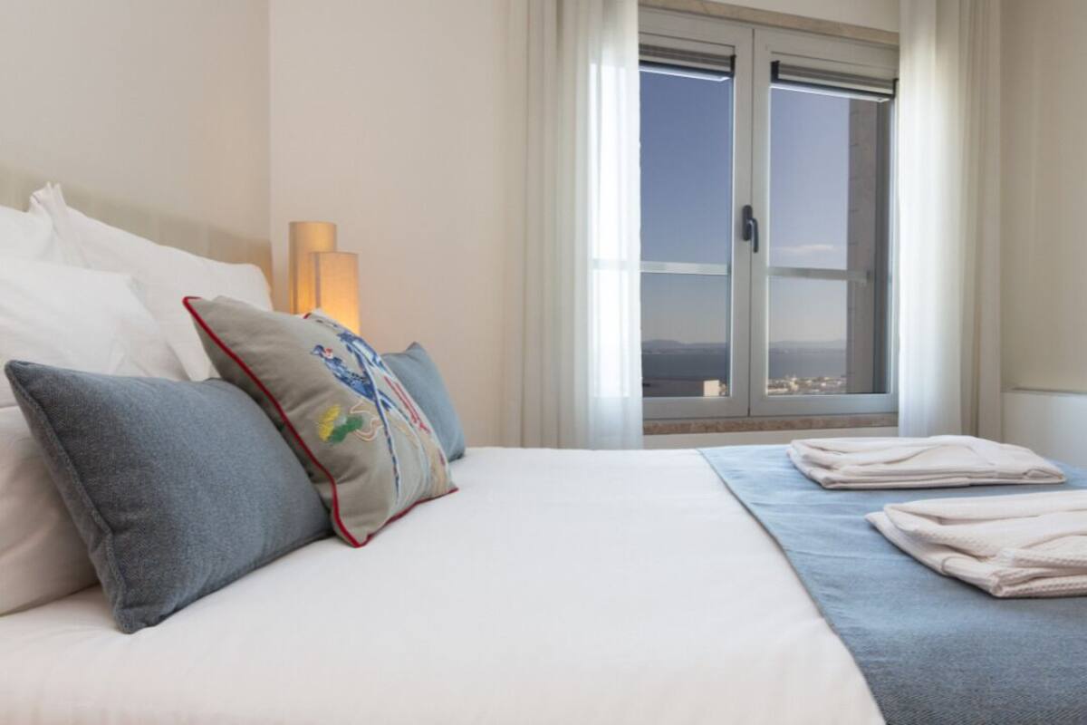 Una habitación de hotel con una cama, almohadas, una ventana con vistas y una lámpara.