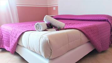 Un letto con una coperta rosa, un asciugamano bianco arrotolato e un fiore viola.