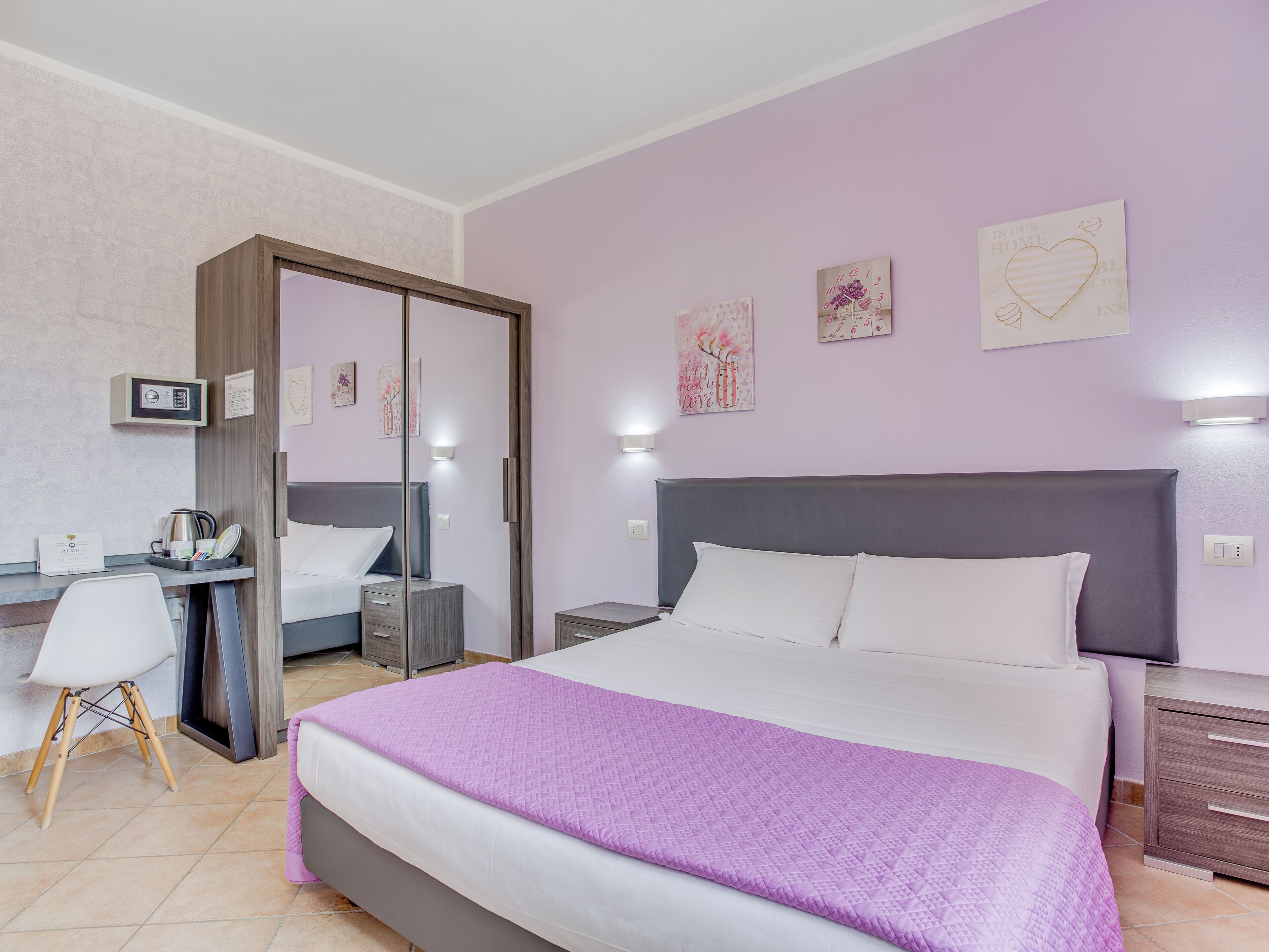 Habitación de hotel con cama, mesitas de noche, escritorio, silla, armario y cuadros en las paredes.