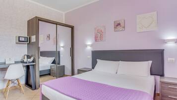 A hotel room with a bed, bedside tables, a desk, a chair, a wardrobe, and artwork on the walls.