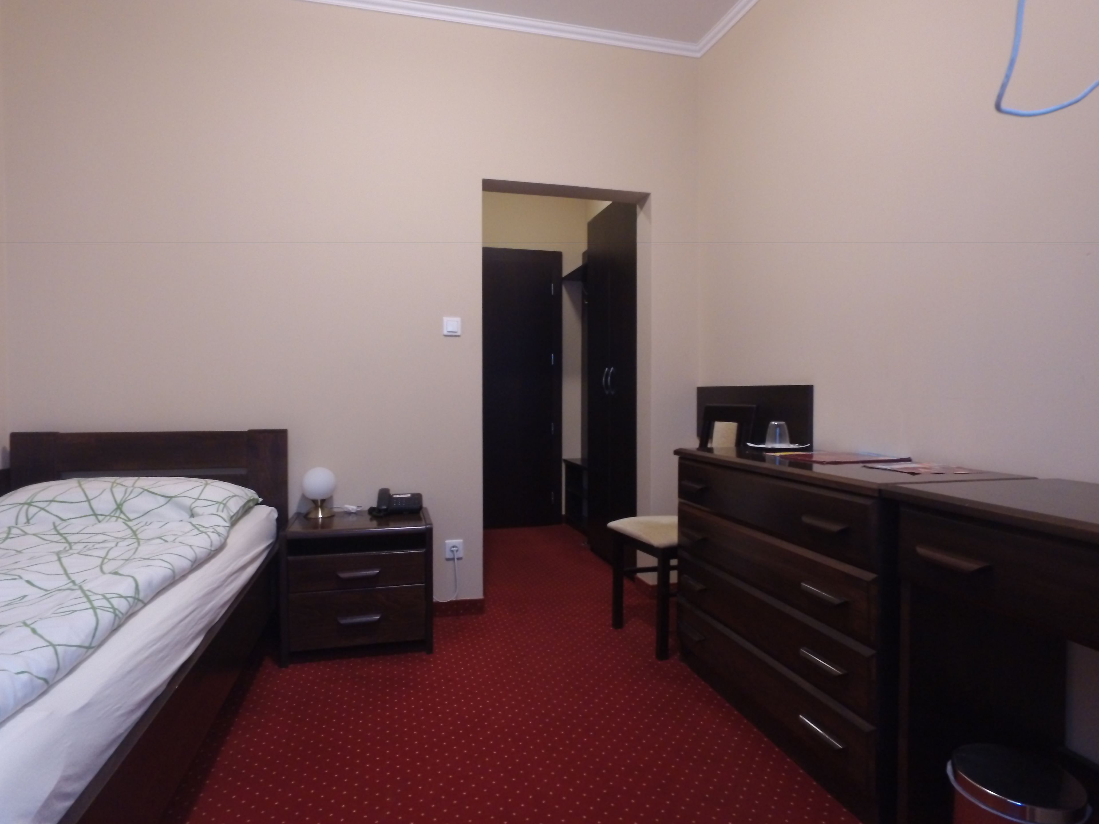 Habitación de hotel con cama, tocador, escritorio y silla. Hay una alfombra roja en el suelo.