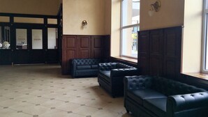 Un hall d’hôtel doté d’une grande fenêtre, d’un canapé de couleur sombre et d’un sol carrelé.