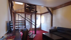 Un salon avec un canapé, une table à manger et des chaises, un escalier et une petite télévision.