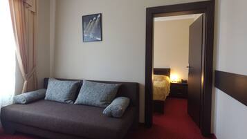 A hotel room with a sofa, a bed, a nightstand, and a door leading to another room.