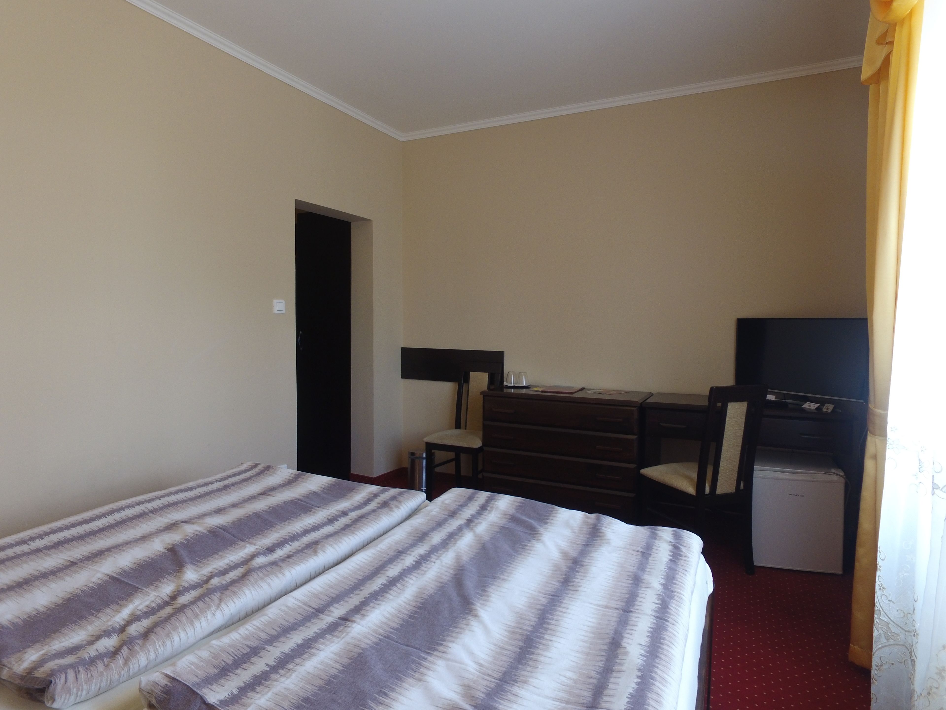 Una habitación de hotel con cama, escritorio, silla, televisor y un refrigerador pequeño.