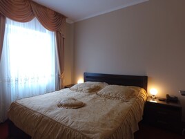 Una habitación de hotel con una cama grande, una mesita de noche con lámpara y una ventana con cortinas.