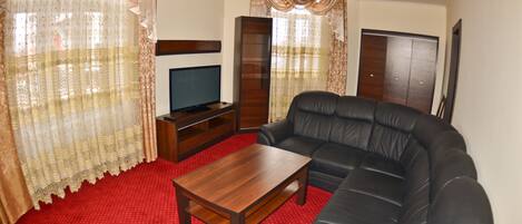 A living room with a black leather sofa, a wooden coffee table, and a television on a stand.
