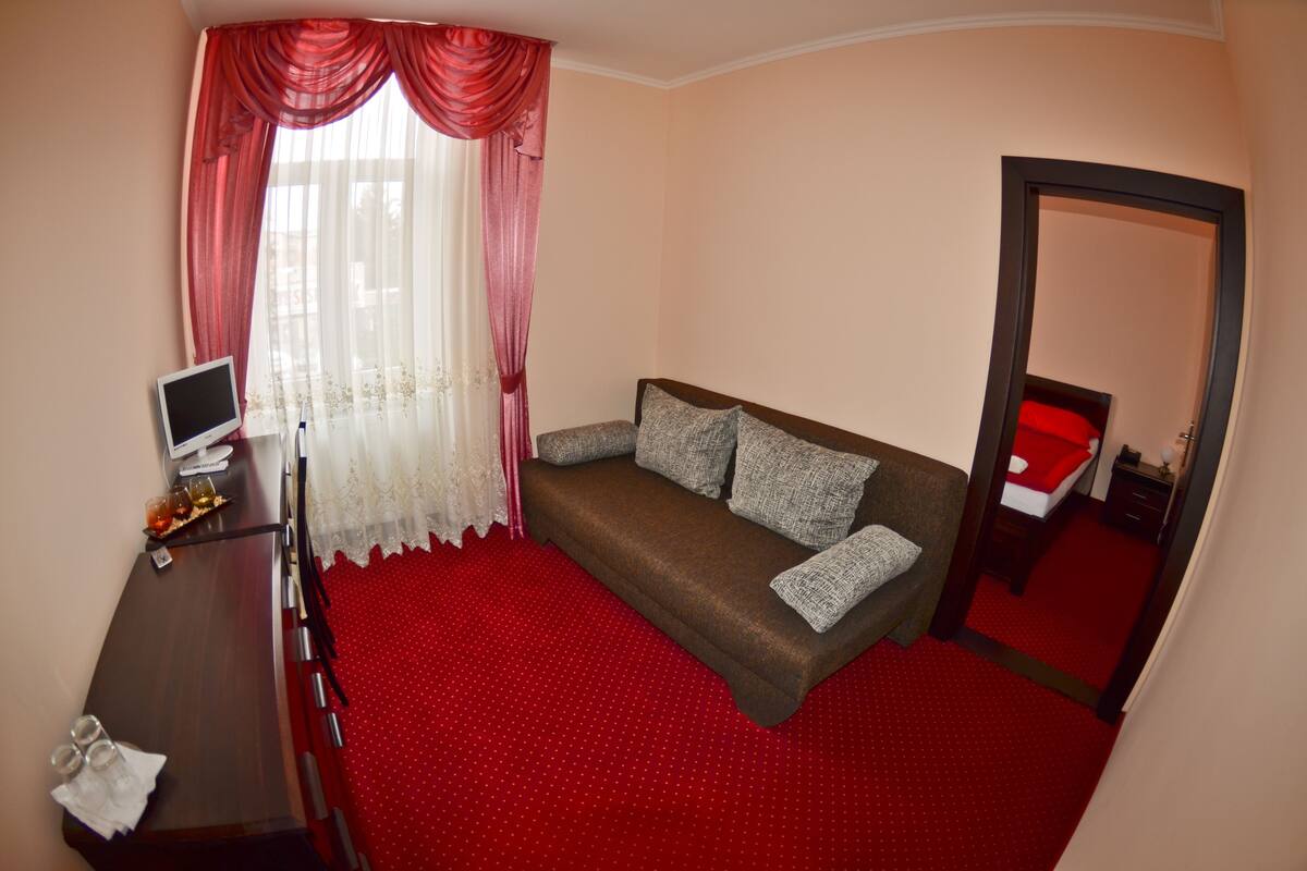 A room with a brown sofa, a TV on a wooden desk, and a red carpet.