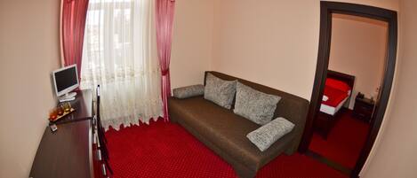 A room with a brown sofa, a TV on a wooden desk, and a red carpet.