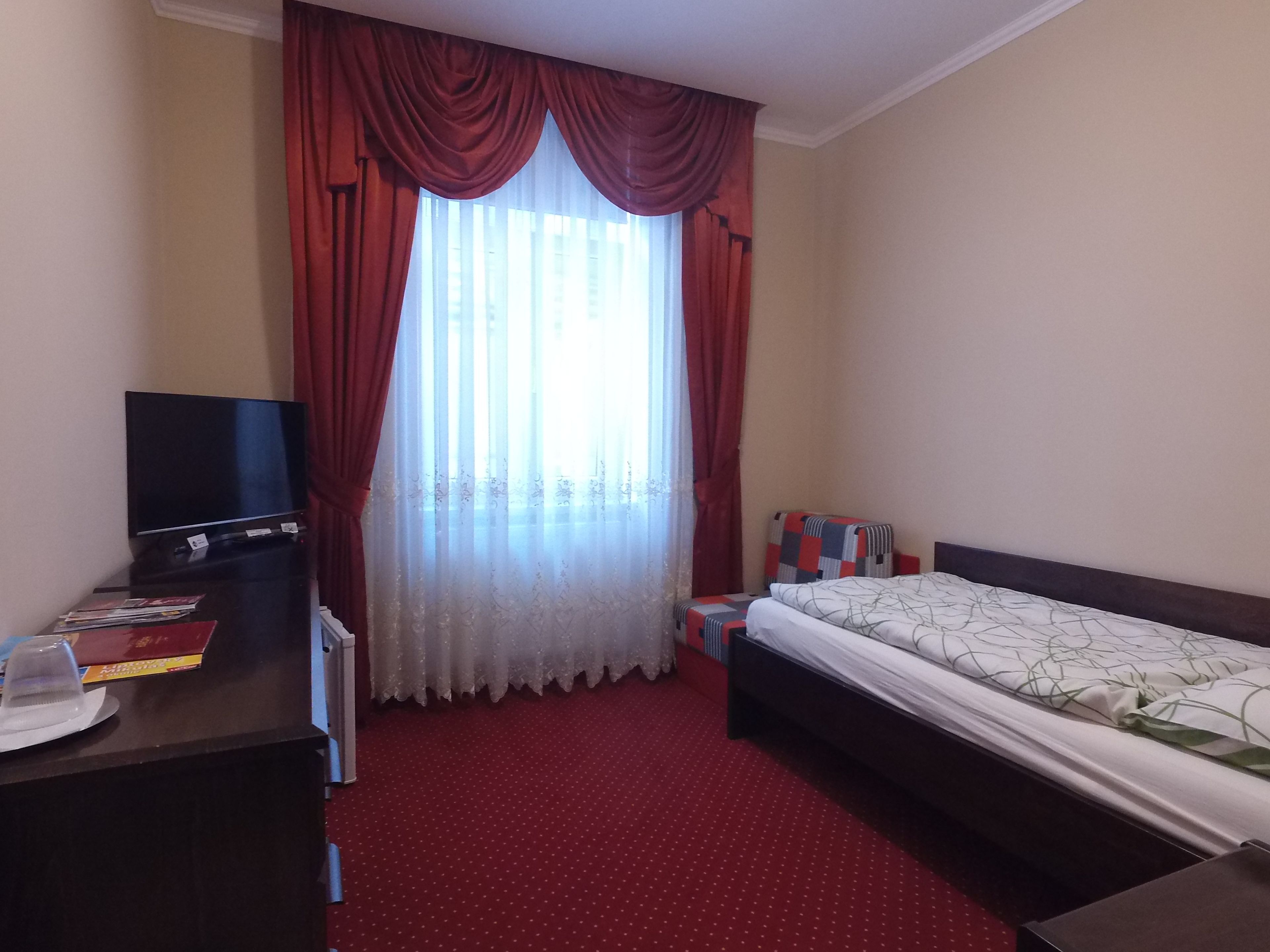 A hotel room with a bed, a desk with a TV, and a window with curtains.