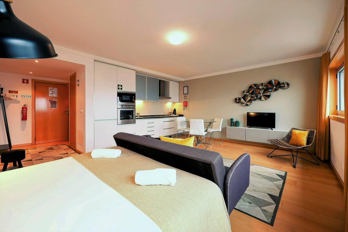 A hotel room with a bed, a desk, a chair, a television, and a kitchenette.
