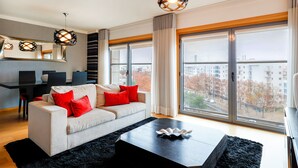 A modern living room with a sofa, a coffee table, and large windows offering a city view. - Oriente 57 Apartments by APT IIN - Parque das Nações (Lisbon)