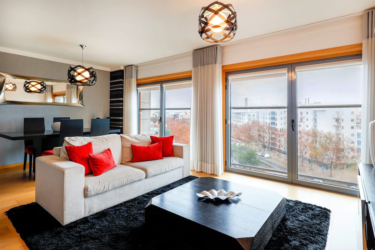 A modern living room with a sofa, a coffee table, and large windows offering a city view.