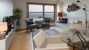 A modern living room with a glass coffee table, two armchairs, a sofa, and a large window offering a view of the sea. - Oriente 57 Apartments by APT IIN - Parque das Nações (Lisbon)