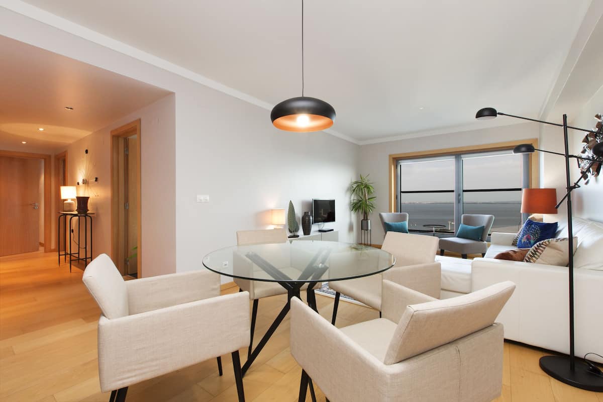 A modern living room with a glass-top coffee table, beige sofas, and a large window offering a view.